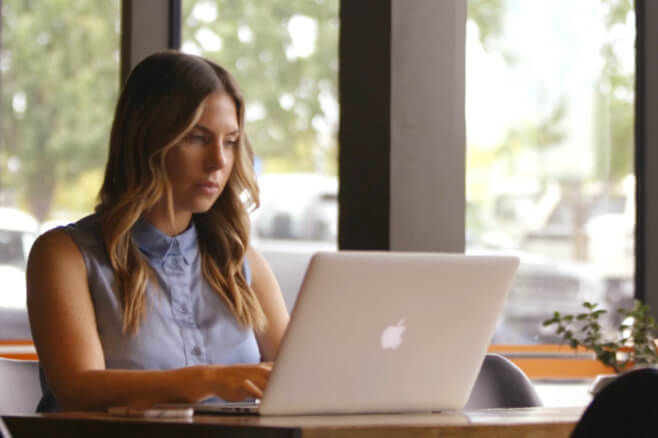 An Alliance Software client working at a table in a coffee shop on their laptop.