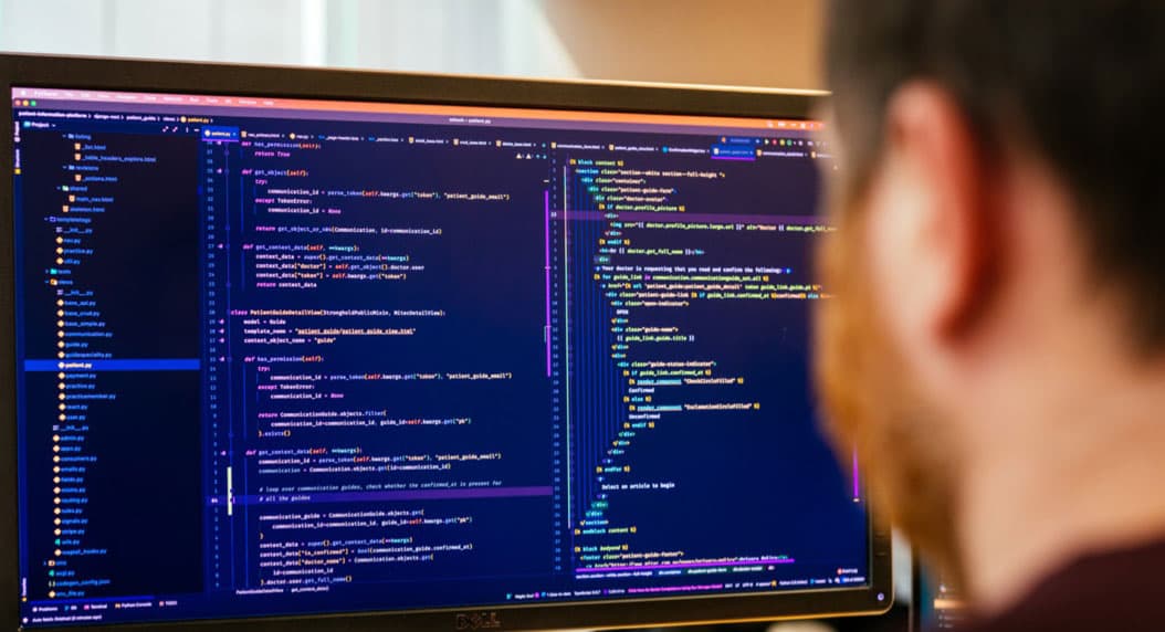 An over the shoulder view of Aaron, one of the developers at Alliance Software. He is looking at a large desktop monitor which is displaying a code editor.