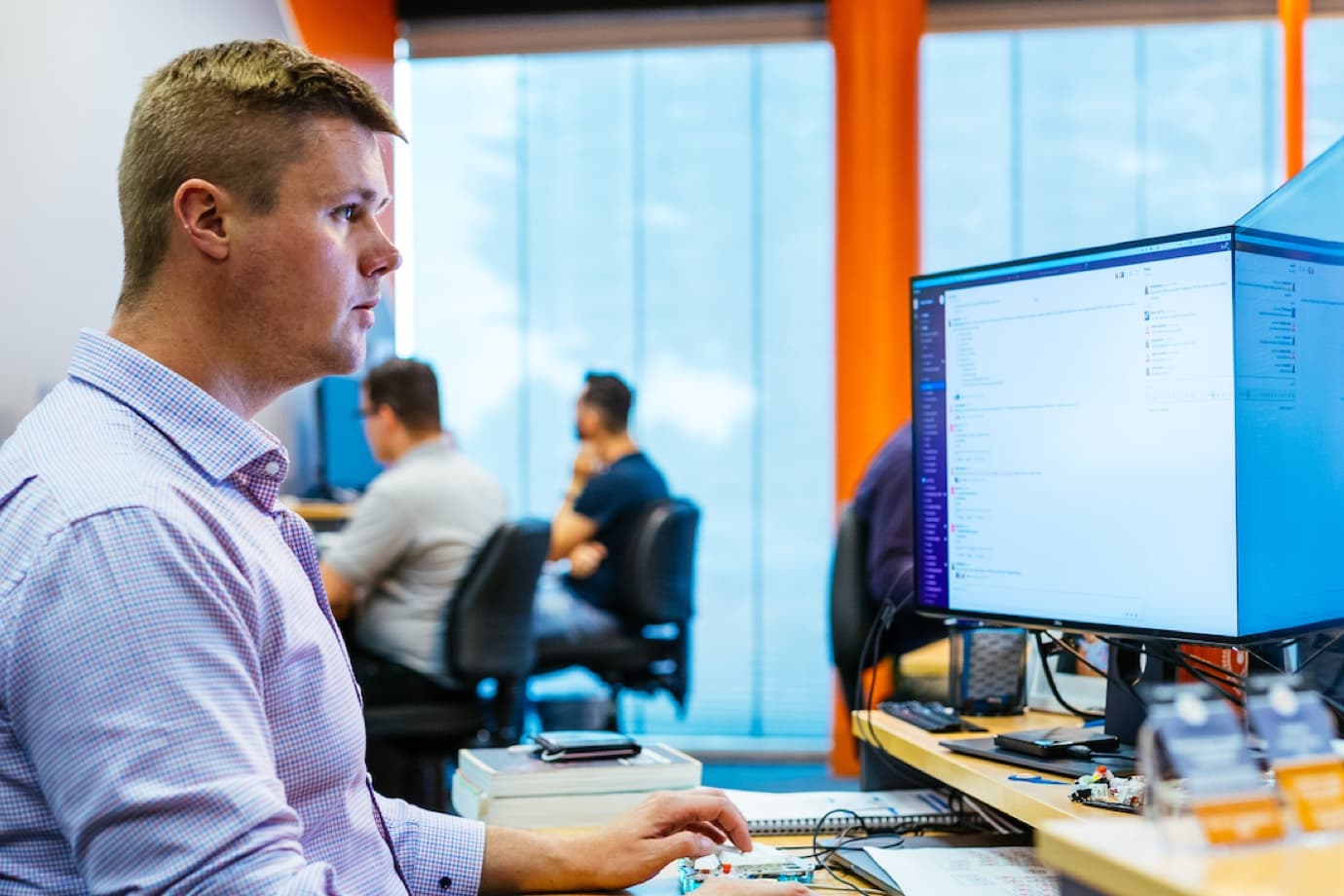 James, an Allince developer in front on a computer coding. Four other developers in the background coding.