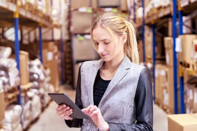 Lady in a warehouse looking at inventory details on a tablet.