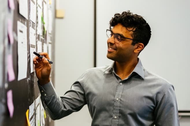 A smiling Naser, one of Alliance Software's project managers, pointing to a wall of documents, viewed from the side.